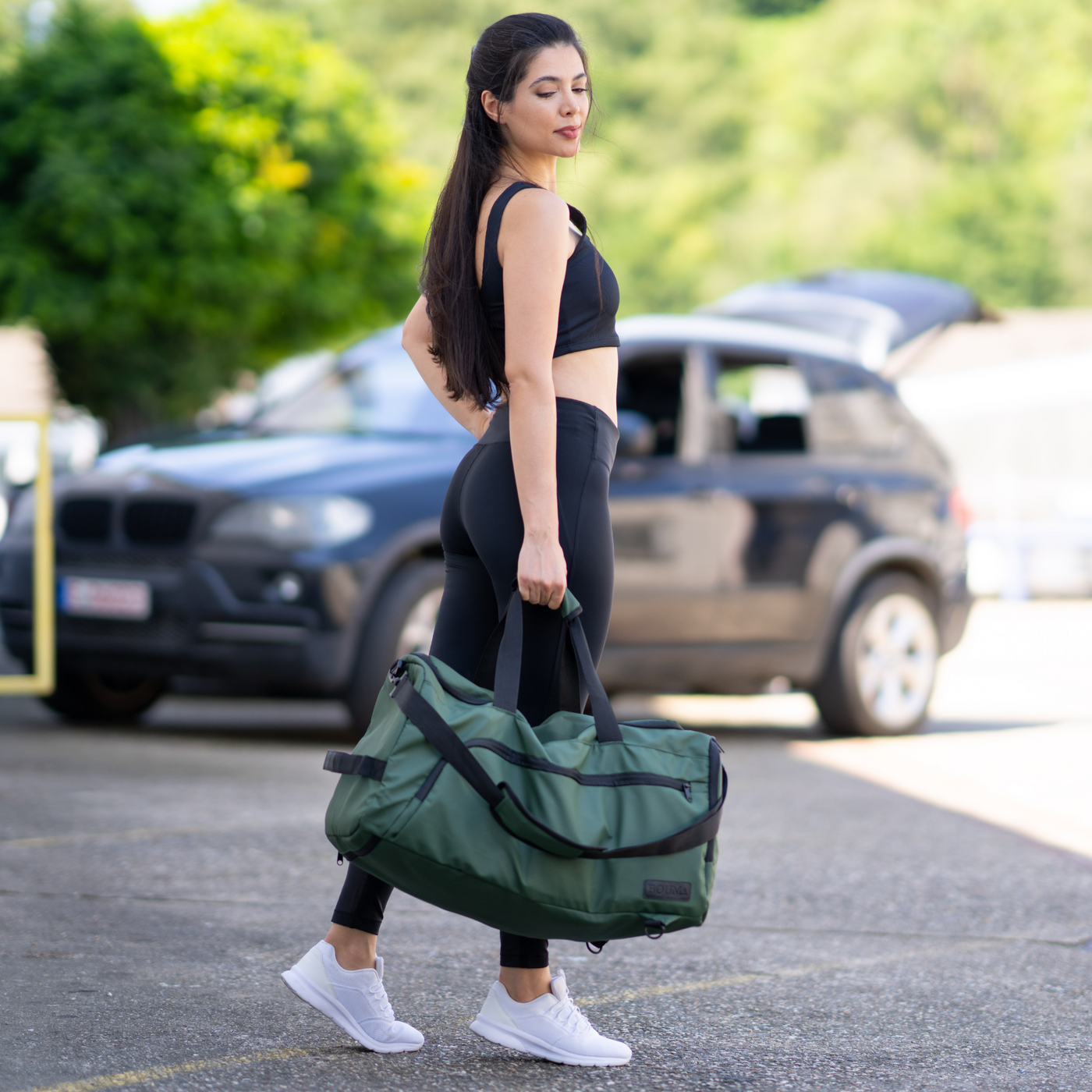 Frau trägt die Organizer Bag XL in Military Green am Tragegriff auf einem Parkplatz